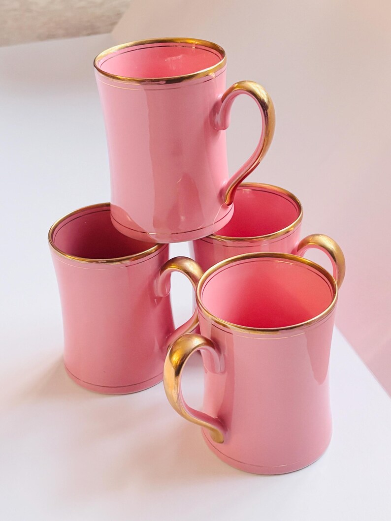 Pu&ograve; includere: Set di quattro tazze in ceramica rosa con bordo dorato. Le tazze hanno una forma arrotondata e un manico.