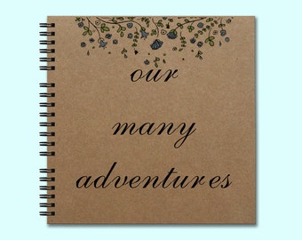 May include: A brown spiral bound journal with a floral design at the top and the text "our many adventures" in black cursive writing.