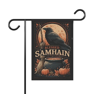 Puede incluir: Una bandera de jardín rectangular colgada en un soporte de metal negro. La bandera muestra un cuervo negro sobre un caldero, una escoba y dos calabazas. El texto BLESSED SAMHAIN está impreso sobre un fondo de una gran luna naranja.