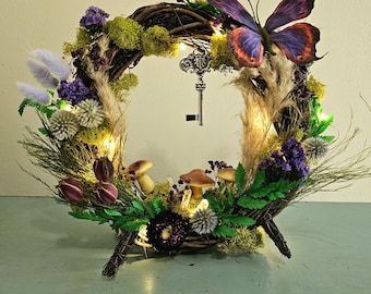 May include: A whimsical wreath decorated with purple flowers, moss, and a butterfly. It features a key charm and fairy lights, creating a magical and enchanting atmosphere.