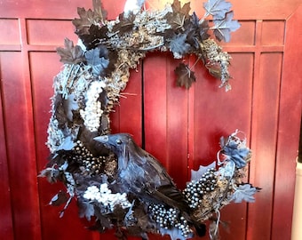 May include: A decorative Halloween wreath featuring a black raven perched on a crescent-shaped base. The wreath is adorned with black leaves, white berries, and dark gray accents, creating a spooky and festive look.