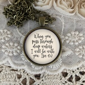 May include: A bronze necklace with a round pendant featuring the text "When you pass through deep waters I will be with you. Isa 43:2" on a white background.