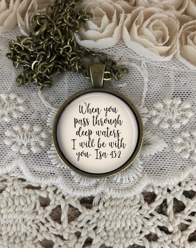 May include: A bronze necklace with a round pendant featuring the text "When you pass through deep waters I will be with you. Isa 43:2" on a white background.
