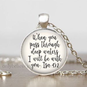 May include: A silver necklace with a round glass pendant featuring the text "When you pass through deep waters I will be with you. Isa 43:2"