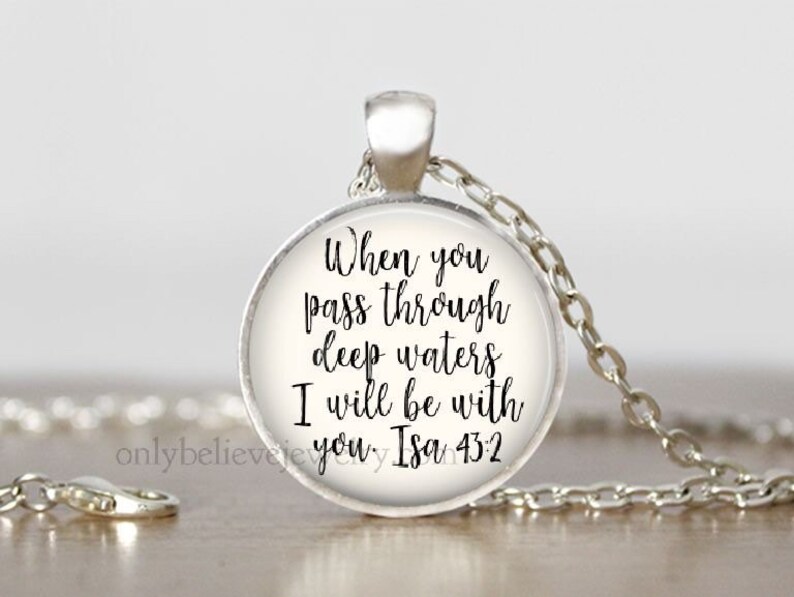 May include: A silver necklace with a round glass pendant featuring the text "When you pass through deep waters I will be with you. Isa 43:2"