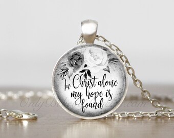 May include: A silver necklace with a round pendant featuring a black and white floral design and the text "In Christ alone my hope is found".