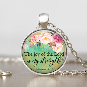 Puede incluir: Un collar de plata con un colgante redondo de vidrio con un dise&ntilde;o floral y la cita "La alegr&iacute;a del Se&ntilde;or es mi fortaleza" con la referencia b&iacute;blica "Nehem&iacute;as 8:10".