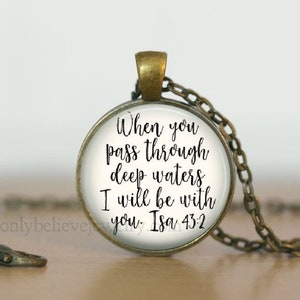 May include: A silver necklace with a round glass pendant featuring the text "When you pass through deep waters I will be with you. Isa 43:2" in black cursive lettering.