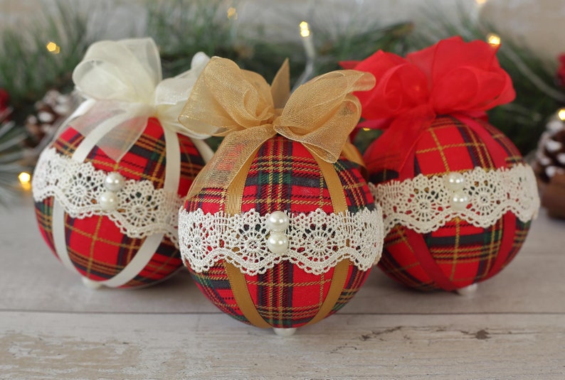 May include: Three red and gold plaid Christmas ornaments with white lace trim and pearl accents. Each ornament has a different colored ribbon bow.