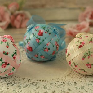 Peut inclure: Trois sph&egrave;res d&eacute;coratives florales avec des rubans. Une sph&egrave;re est rose clair avec un ruban rose, une autre est bleu clair avec un ruban bleu, et la troisi&egrave;me est cr&egrave;me avec un ruban cr&egrave;me. Chaque sph&egrave;re a un motif floral avec des roses rouges et roses.