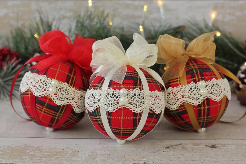 May include: Three red, white, and gold plaid Christmas ornaments with white lace trim and pearl accents. Each ornament has a different colored ribbon bow.