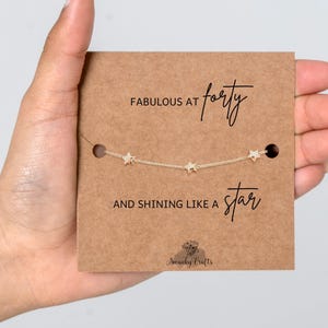 May include: A gold-toned chain bracelet featuring three small star charms, displayed on a rectangular brown card. The card text reads FABULOUS AT forty AND SHINING LIKE A star, with the logo Swanky Crafts printed at the bottom center.
