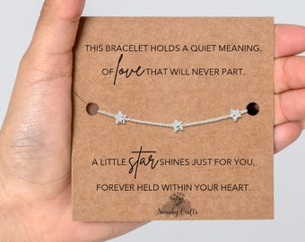 Könnte beinhalten: Ein silberfarbenes Kettenarmband mit drei kleinen Sternanhängern, präsentiert auf einer rechteckigen braunen Karte mit schwarzem Textaufdruck: THIS BRACELET HOLDS A QUIET MEANING, OF love THAT WILL NEVER PART. A LITTLE star SHINES JUST FOR YOU, FOREVER HELD WITHIN YOUR HEART. Swanky Crafts.