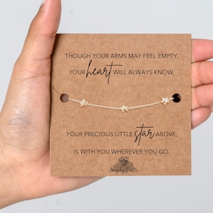 May include: A gold star necklace on a brown card with the text "Though your arms may feel empty, your heart will always know, your precious little star above, is with you wherever you go." The brand name "Swanky Crafts" is at the bottom.