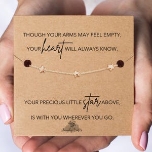 May include: A gold-coloured star necklace on a brown card with the text: "Though your arms may feel empty, your heart will always know, your precious little star above, is with you wherever you go." The brand name "Swanky Crafts" is also visible.