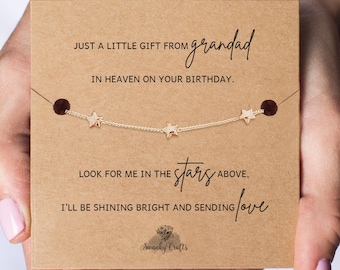 Könnte beinhalten: Ein zartes, goldfarbenes Kettenarmband mit drei kleinen Sternanhängern, präsentiert auf einer quadratischen Karte aus Kraftpapier. Die Karte enthält den gedruckten Text: JUST A LITTLE GIFT FROM grandad IN HEAVEN ON YOUR BIRTHDAY. LOOK FOR ME IN THE stars ABOVE, I'LL BE SHINING BRIGHT AND SENDING love. Das Swanky Crafts Logo befindet sich unten.