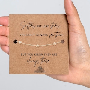 May include: A delicate gold-tone chain bracelet featuring three small star charms, mounted on a square brown card. The card displays the text: Sisters are like stars, you don't always see them, but you know they are always there. Swanky Crafts.
