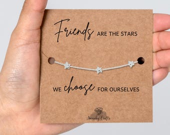 May include: A silver-toned chain bracelet featuring three small star charms, displayed on a rectangular brown card. The card text reads: Friends ARE THE STARS WE choose FOR OURSELVES, with the Swanky Crafts logo printed at the bottom.