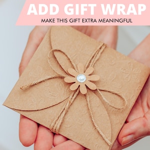May include: A brown gift envelope with a flower embellishment and twine. The envelope is decorated with a floral pattern and tied with twine. The flower has a rhinestone centre. Text at the top reads "ADD GIFT WRAP MAKE THIS GIFT EXTRA MEANINGFUL."