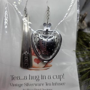 May include: A vintage silverware tea infuser in the shape of a heart and a spoon. The infuser is made of silver-colored metal and is packaged in a clear plastic sleeve. The text on the packaging reads "Tea...a hug in a cup!" and "Vintage Silverware Tea Infuser by Rose Petal Designs."