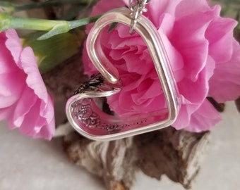 May include: A silver heart-shaped pendant necklace made from a vintage spoon, with floral details, hanging against a pink flower.