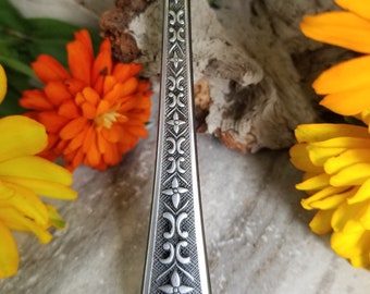 May include: A silver spoon pendant necklace with an ornate floral design. The spoon is attached to a silver chain.