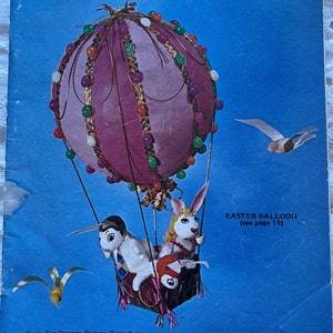 May include: A vintage magazine cover for Pack-o-Fun, a scrap-craft magazine. The cover features a pink and white Easter balloon with two bunny puppets hanging from it. The magazine cover is blue with the title "Pack-o-Fun" in white letters. The text "The Only Scrap-Craft Magazine" is also in white letters. The magazine cover also includes the text "Easter Balloon (see page 15)" and "April 1971".