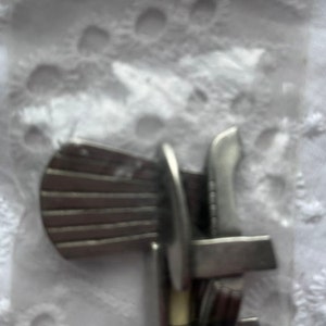May include: A silver watch band clasp with a spring-loaded mechanism. The clasp has a textured surface and a polished finish.