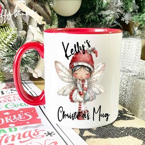 May include: A white ceramic mug with a red interior and handle. The mug features a Christmas fairy illustration and the text "Kelly's Christmas Mug". Festive holiday decor is in the background.