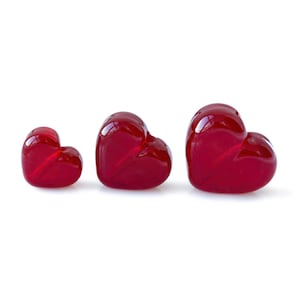 May include: Three red glass hearts of different sizes. The hearts are arranged in a row from smallest to largest.