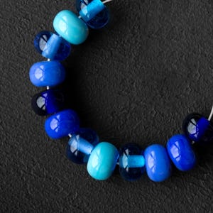 May include: A strand of blue and turquoise glass beads, strung on a white thread. The beads are arranged in a gradient, with the darkest blue beads at one end and the lightest turquoise beads at the other.