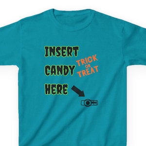 以下が含まれることがあります： 緑色の「INSERT CANDY HERE」とオレンジ色の「TRICK OR TREAT」の文字が入ったターコイズ色のTシャツ。黒い矢印がキャンディディスペンサーのグラフィックを指しています。楽しいハロウィーンをテーマにしたTシャツ。