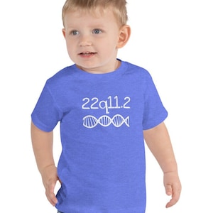 May include: A toddler wearing a blue t-shirt with the text "22q11.2" and a white DNA strand graphic. The shirt is made of a soft, comfortable material.