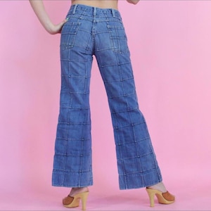 May include: Blue denim flared pants with a unique design featuring multiple stitched squares. The pants have a high waist and a wide leg.