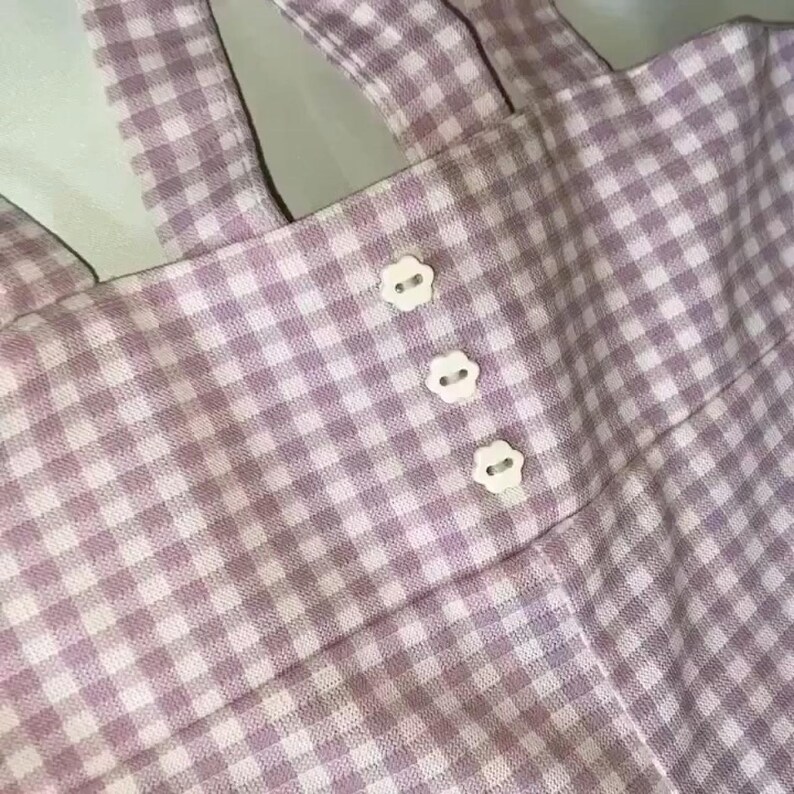 May include: Pink and white gingham fabric with three white buttons.