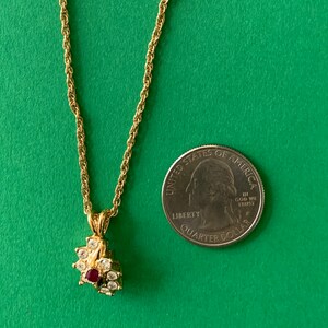 May include: A gold chain necklace with a small pendant featuring a red and clear rhinestone flower design. The pendant is about the size of a quarter.