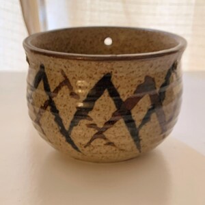 May include: A small, brown ceramic hanging planter with a geometric pattern of black and brown diamonds. The planter has a hole for drainage.
