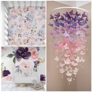 K&ouml;nnte beinhalten: Ein wei&szlig;es Babybett mit einem floral gemusterten Bettuch und einem rosa, lila und wei&szlig;en Schmetterlingsmobile, das dar&uuml;ber h&auml;ngt. Das Mobile hat einen Holzring und besteht aus Papierschmetterlingen.
