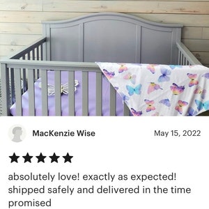 K&ouml;nnte beinhalten: Ein lila und pinkfarbener Schmetterlingsmobile h&auml;ngt &uuml;ber einem Kinderbett mit einem wei&szlig;en und lilafarbenen Schmetterlingsmuster. Das Mobile besteht aus Papierschmetterlingen und ist eine tolle Erg&auml;nzung f&uuml;r ein Kinderzimmer.