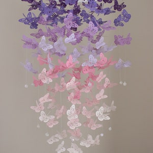 K&ouml;nnte beinhalten: Ein Mobile aus Papier in Form von Schmetterlingen in Lila, Lavendel und Rosa mit Kristallperlen, die an einem wei&szlig;en Metallring h&auml;ngen.  "Monkey Nut Design" steht in der oberen rechten Ecke des Bildes.