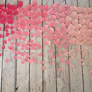 May include: A collection of pink heart-shaped decorations in varying shades, arranged on a weathered, light-colored wooden surface. The hearts transition from deep pink to a lighter, pastel hue, creating a gradient effect.