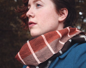 May include: A woman with short, red hair wearing a blue jacket and a striped scarf. The scarf is brown, orange, and white.