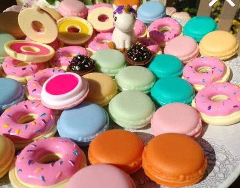 May include: A collection of small, round, colorful plastic containers shaped like donuts and macarons, featuring pastel and bright shades of pink, blue, green, orange, and yellow. A small white unicorn figurine with a purple mane sits among the items.