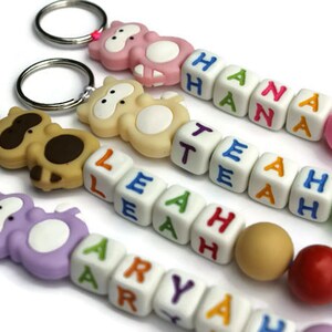 May include: Four colorful keychains with animal charms and letter beads spelling out the names "Aryah", "Leah", "Tea", and "Hana". Each keychain has a different colored animal charm and a variety of colored beads.