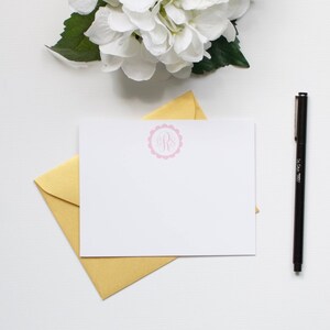 Könnte beinhalten: Eine weiße Karte mit einem rosafarbenen Monogramm in einem Kreisdesign. Die Karte liegt auf einem goldenen Umschlag.