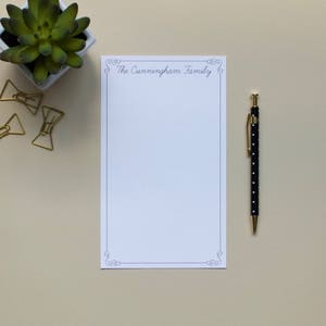 May include: A white notepad with a decorative border and the text "The Cunningham Family" at the top. A black pen with white polka dots is next to the notepad.