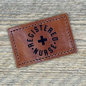 May include: Brown leather patch with white stitching and the text "REGISTERED NURSE" in a circle with a black plus sign in the center.