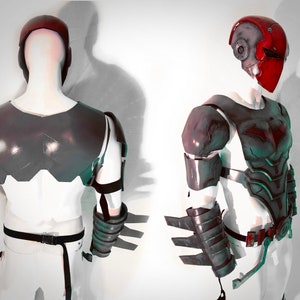 May include: A black and grey costume armour with a red helmet. The armour has a textured surface and is made of a hard material. The helmet has a visor and a red paint job.