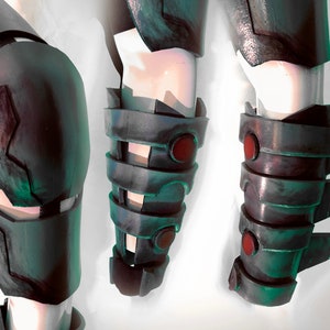 May include: Three close-up views of a dark grey and green metal forearm armour piece with red accents. The armour has a segmented design with a series of plates and a pointed edge.