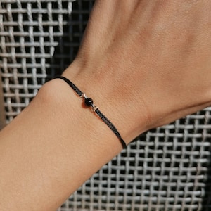 Op de afbeelding: Een eenvoudige zwarte armband van touw met een enkele zwarte kraal.